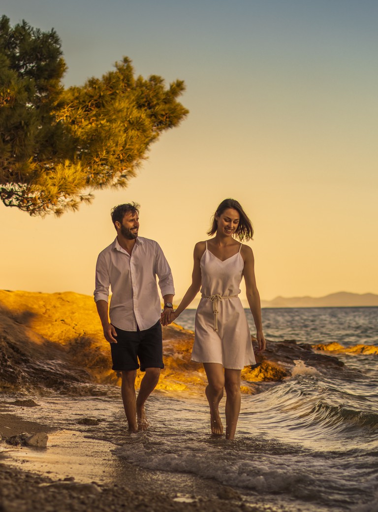 Romantični par šeta uz plažu u zalazak sunca u Orebiću, Hrvatska, blizu Aminess Younique Bellevue Hotela.