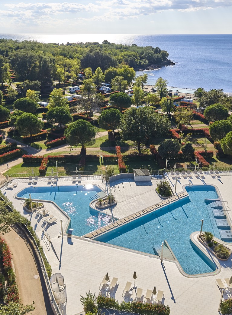 Panoramski pogled na bazen in plažo v Aminess Planet Camping Maravea Resort, obdano z zelenjem, popolno mesto za sprostitev in uživanje v počitnicah