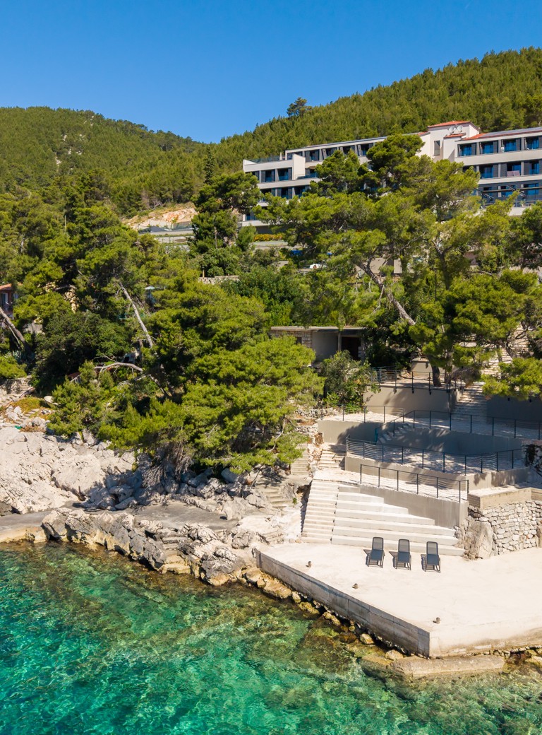 Widok z lotu ptaka na Aminess Alfir Hotel nad skalistą plażą i turkusowym morzem.