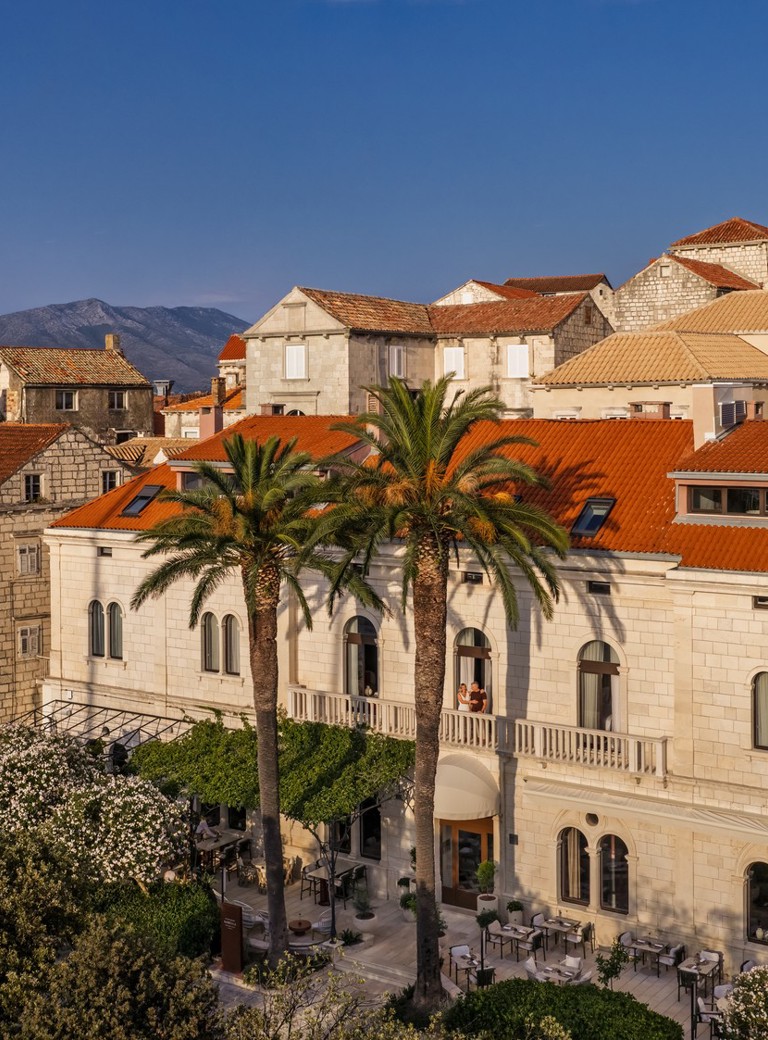 Historic stone Aminess hotel by the sea with palm trees and red roofs.
