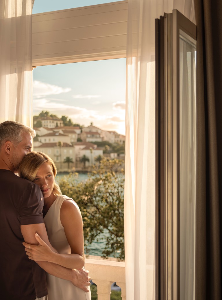 Par se grli uz otvoreni balkon hotela Aminess Younique Korčula Heritage u sumrak.