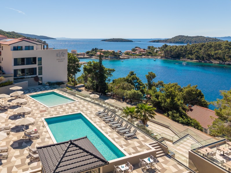 Pools des Aminess Alfir Hotels mit Blick auf türkisblaues Meer und bewaldete Küste.