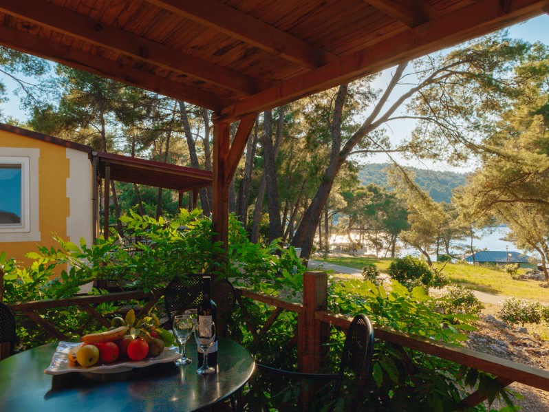 Terrazza della casa per le vacanze Seaside presso Port9 Planet Camping by Aminess, con tetto in legno, vegetazione lussureggiante e vista parziale sul mare.
