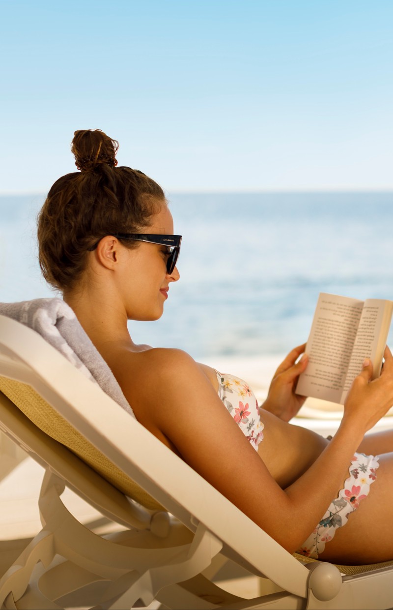 Frau entspannt sich und liest ein Buch am ruhigen Meer während des Sommerurlaubs in einem Aminess Resort