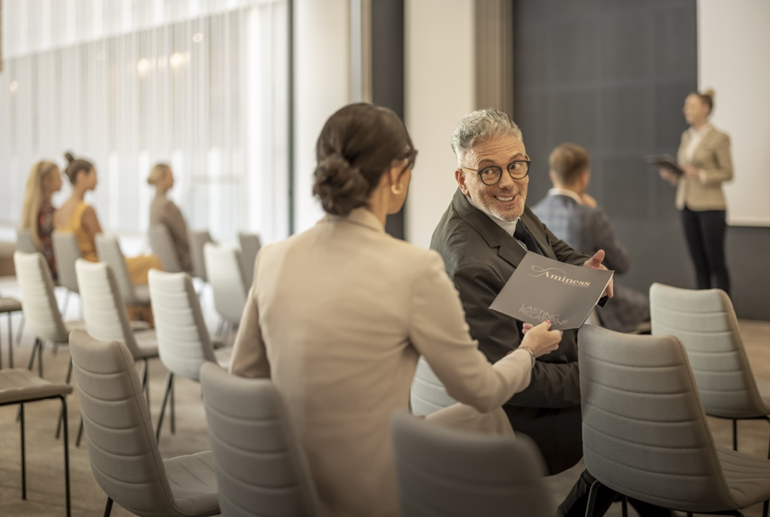 Poslovni događaj s prezentacijom i sudionicima koji sjede u konferencijskoj sali.