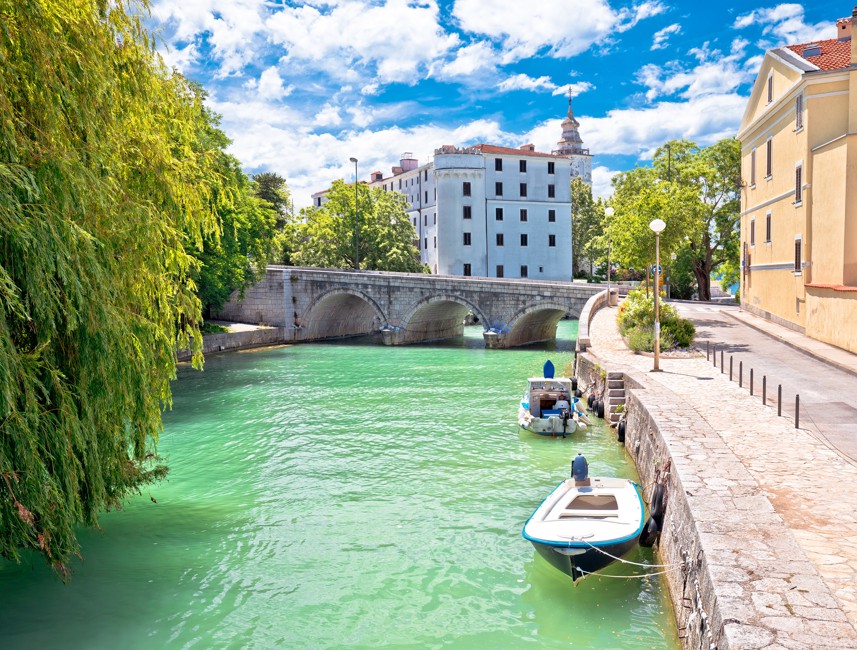 Scenic view of the remains of the Pauline Monastery in Kaštel, Crikvenica, Croatia, with a stone bridge and boats along the river.