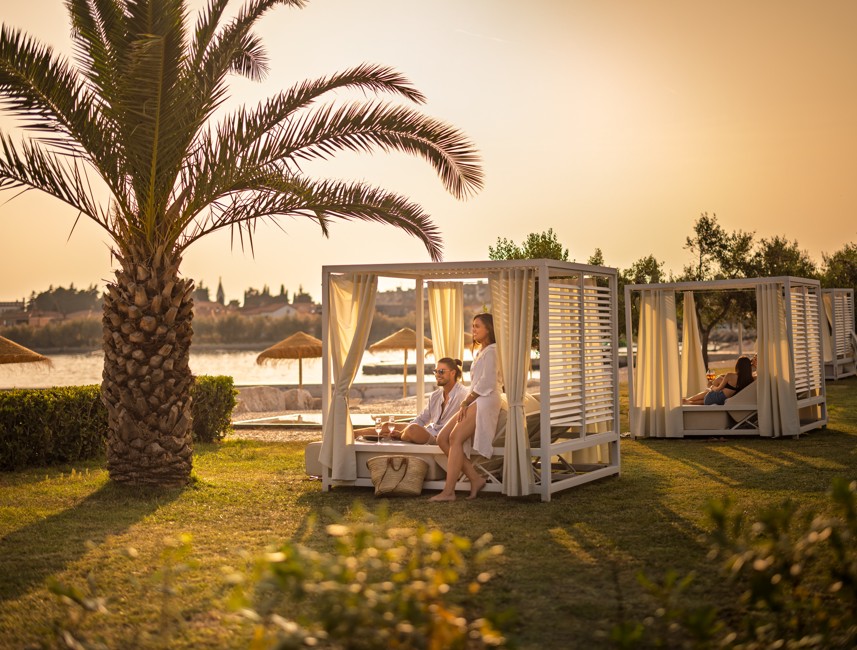 Gast ontspant in een privé cabana omringd door palmbomen bij de Aminess bar in Novigrad, Istrië.