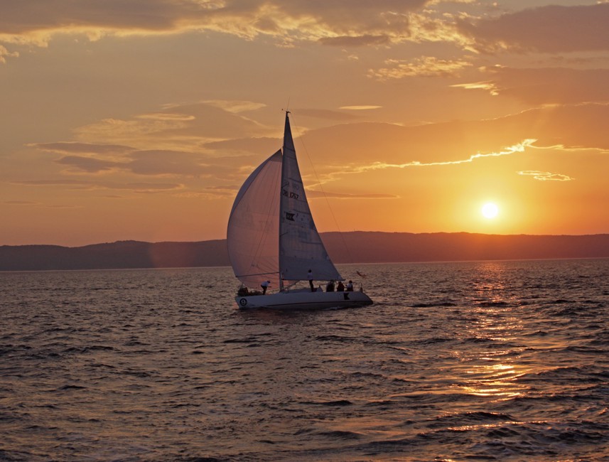 Sailboat gliding across the sea at sunset near Novi Vinodolski, Croatia, with golden skies and calm sea.