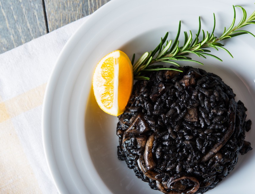 Black squid ink risotto garnished with rosemary and lemon on a white plate in Crikvenica, Croatia.
