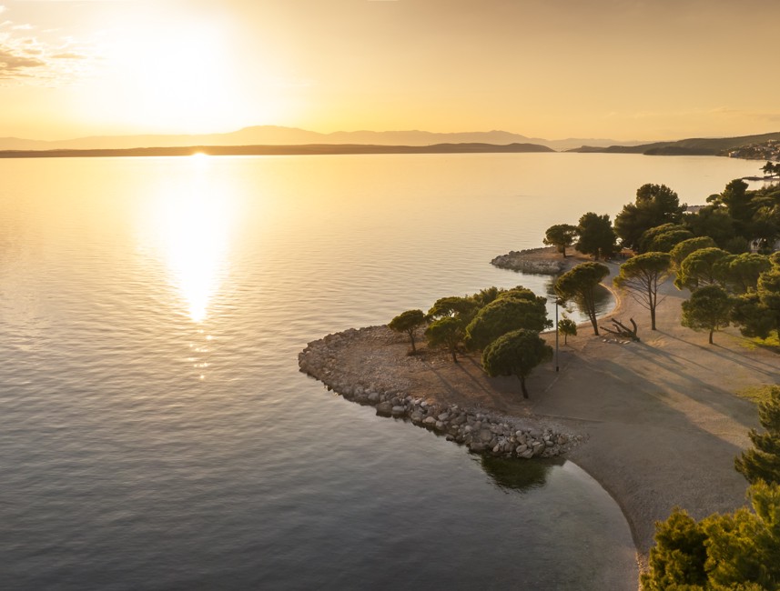 Sunset view over a calm beach with golden light and tree-lined shoreline in Crikvenica.