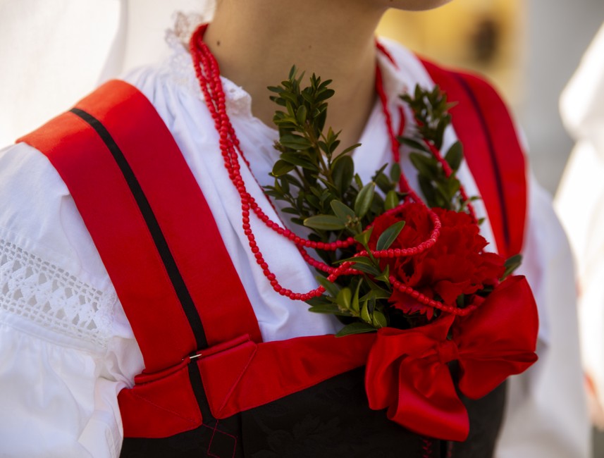 Traditional costume from Novi Vinodolski, Croatia, featuring red and white embroidery with decorative greenery.