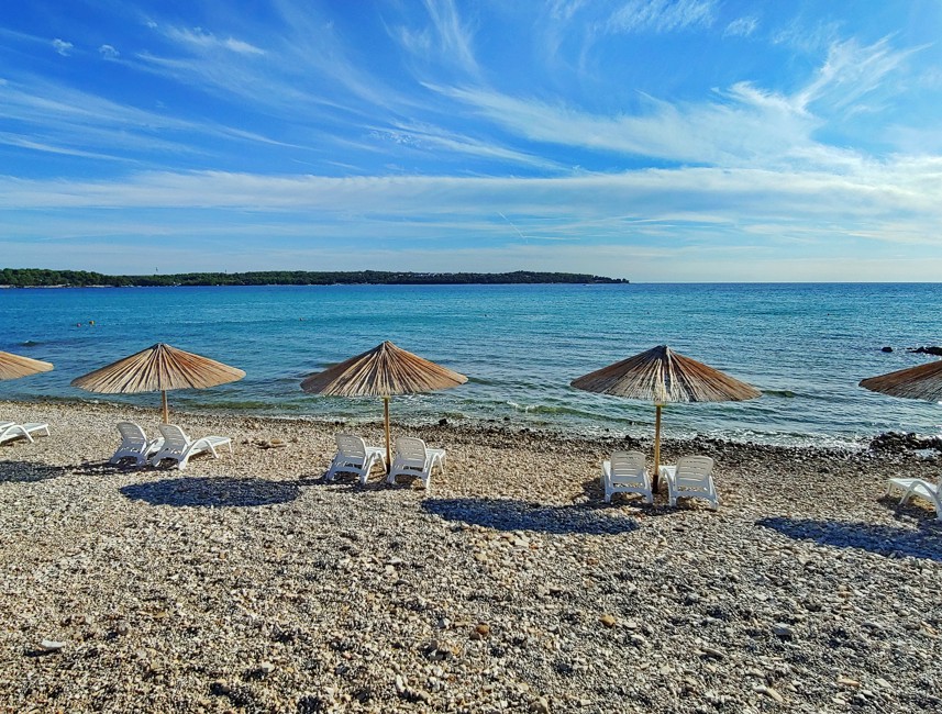 Kieselstrand mit Sonnenschirmen im Aminess Planet Camping Sirena in Novigrad, Kroatien