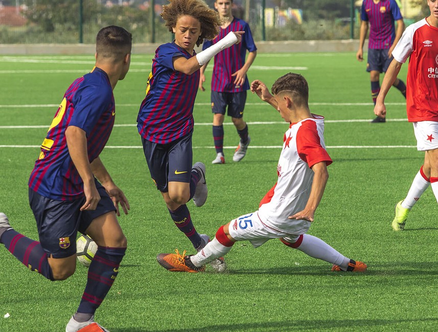 Junge Fußballer, die während eines Spiels auf einem grünen Kunstrasenplatz um den Ball kämpfen.