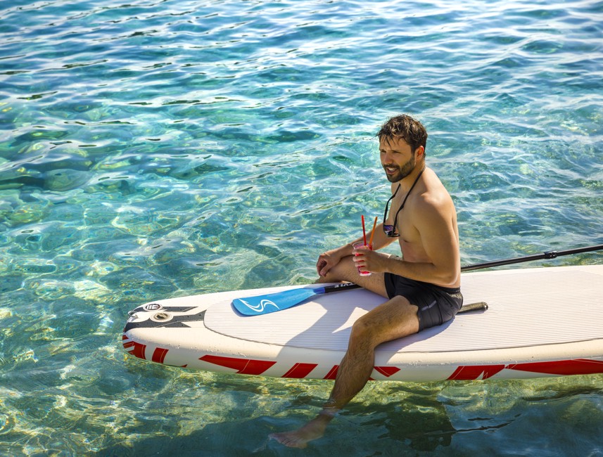 Ein Mann genießt Stand-Up-Paddleboarding in den klaren türkisfarbenen Gewässern in der Nähe von Aminess Port9 Planet Camping Korcula, umgeben von friedlicher Naturlandschaft