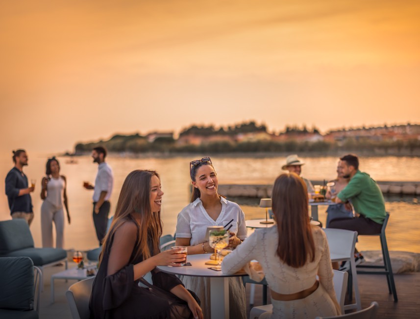 Groep vrienden geniet van drankjes bij de infinity pool bar tijdens zonsondergang bij Aminess in Novigrad, Istrië.