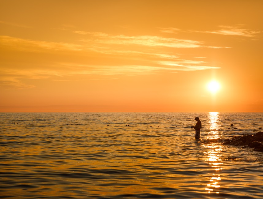 Een visser die vanaf de kust vist met een zonsondergang op de achtergrond