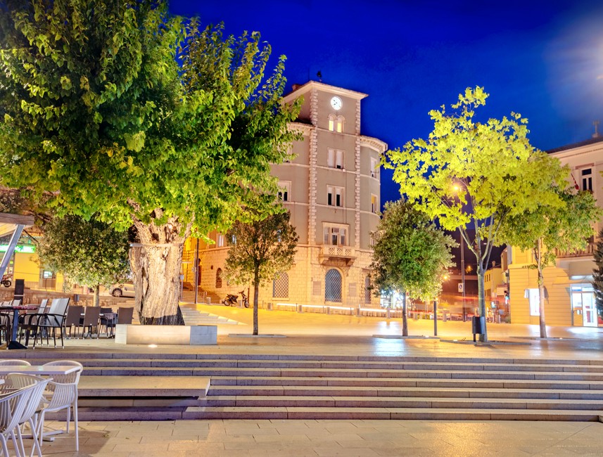 Evening view of a square in Crikvenica, Croatia, illuminated with soft lights and surrounded by historic architecture.