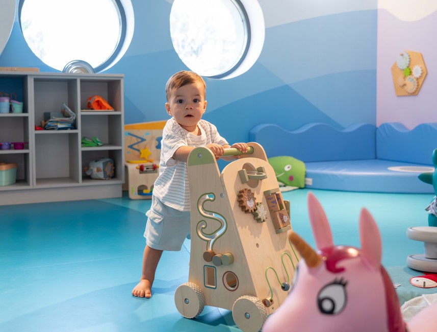Een kind speelt met een houten loopwagen in een kleurrijke speelkamer op Aminess gezinsvakantie.