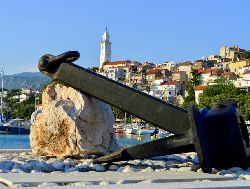Historic anchor at the harbor in Novi Vinodolski, Croatia, with the town and bell tower in the background.