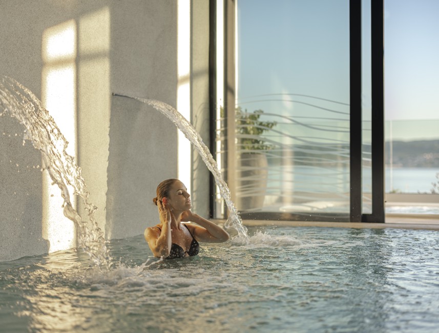 Woman enjoying a soothing waterfall in the pool at Aminess Younique Narrivi Hotel.