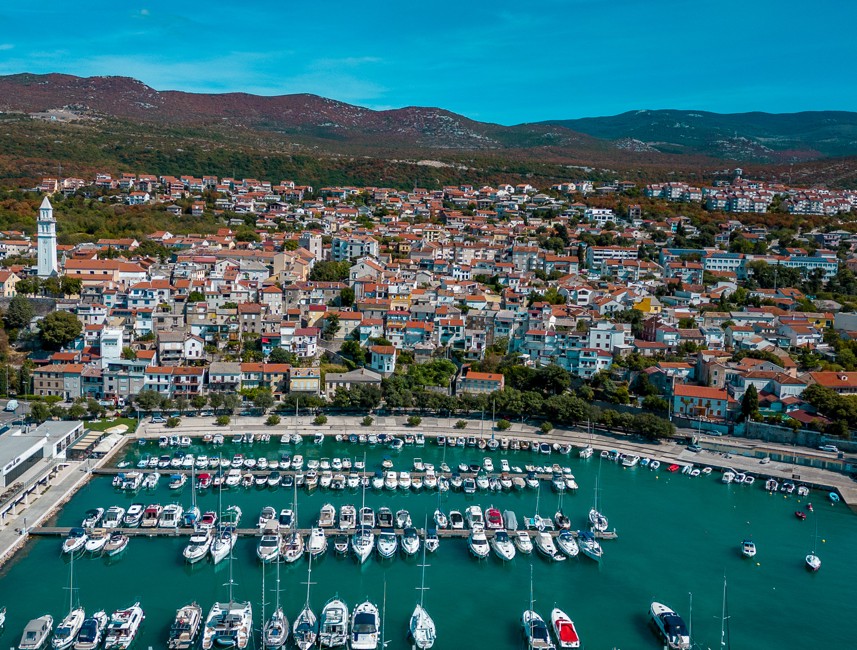 Aerial view of Novi Vinodolski town and marina, Croatia, with boats docked and surrounding hills.