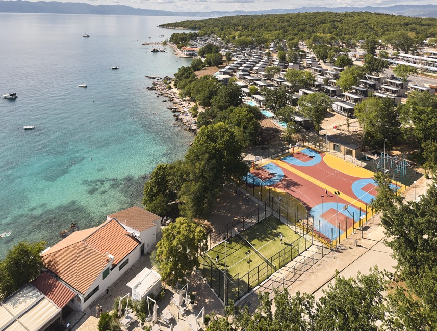 Blick auf das neue, lebendige Sportzentrum des Resorts, mit Plätzen umgeben von üppigem Grün und der ruhigen Adriaküste im Aminess Style Camping Atea Resort.