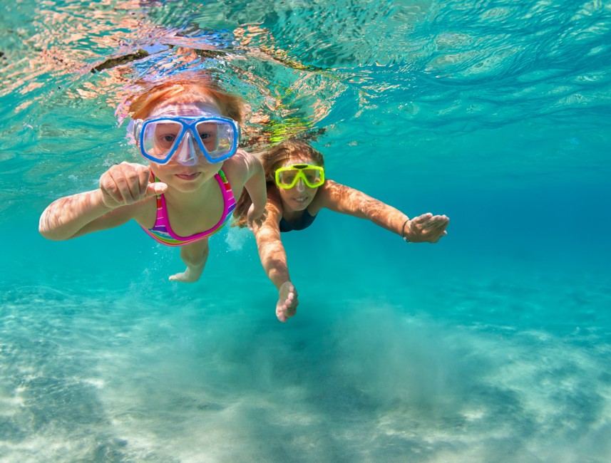 Two children swimming underwater in crystal-clear sea at a beach in Novi Vinodolski, Croatia.