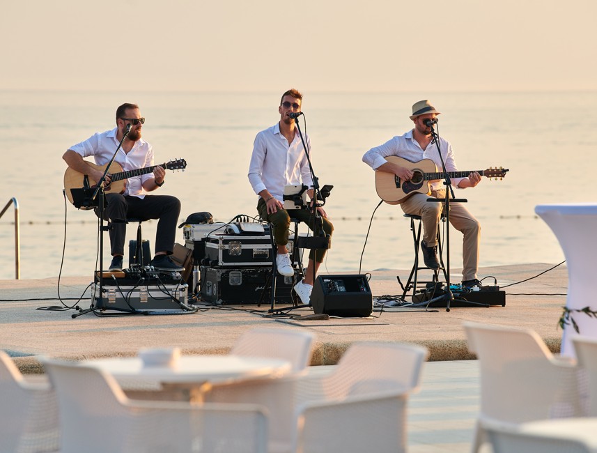 Wedding band performing on a lit stage, with the sea in the background.