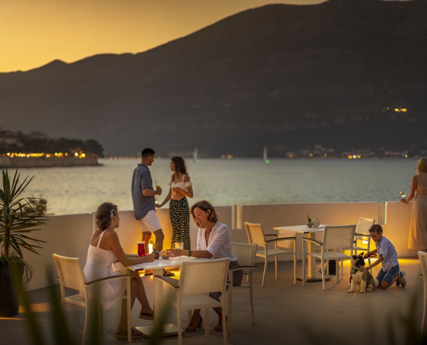 Gäste genießen ein abendliches Beisammensein auf einer Terrasse am Meer bei Sonnenuntergang in einem Aminess Resort