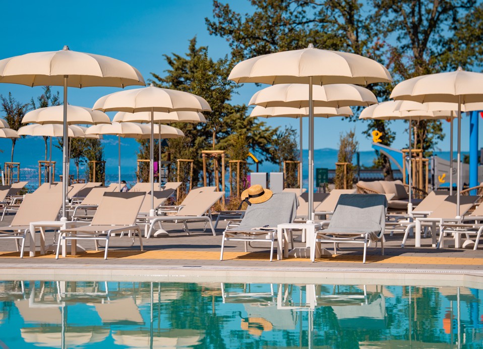 Zona piscina con lettini e ombrelloni beige con vista mare presso l'Aminess Style Camping Atea Resort.