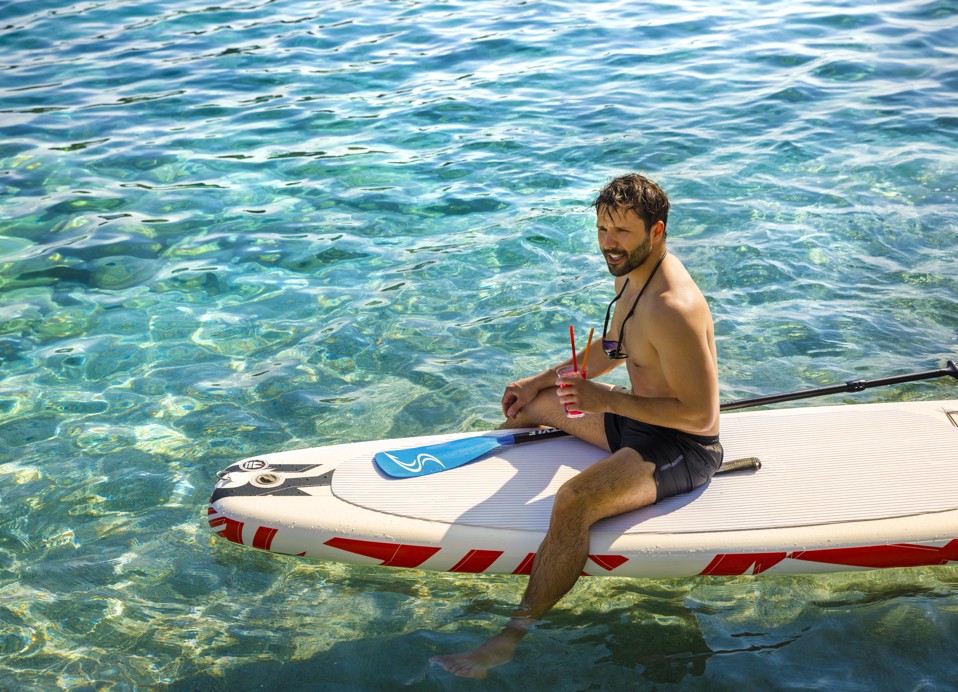 Een persoon die geniet van stand-up paddleboarding in kristalhelder turquoise wateren nabij Korcula, met weelderige omgeving op de achtergrond nabij Maradiso Marko Polo door Aminess.