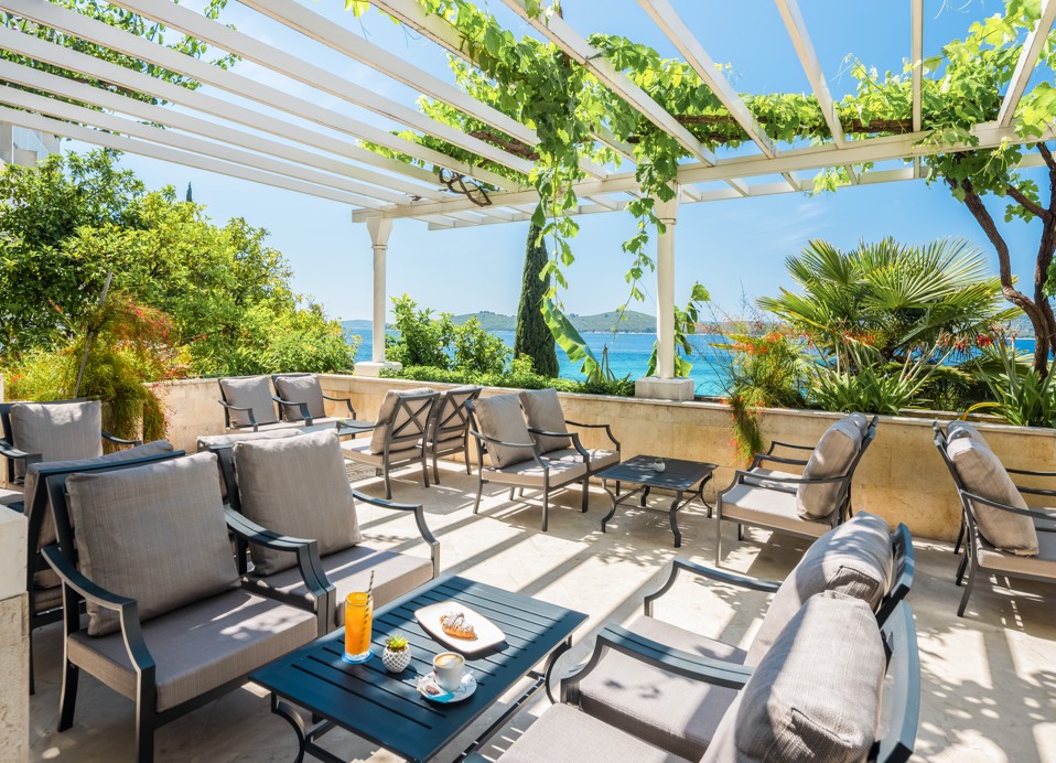 A sun-drenched pool terrace near Orsan by Aminess Hotel in Crotia, offering stunning sea views and comfortable loungers for relaxation nestled among lush mediterranean greenery