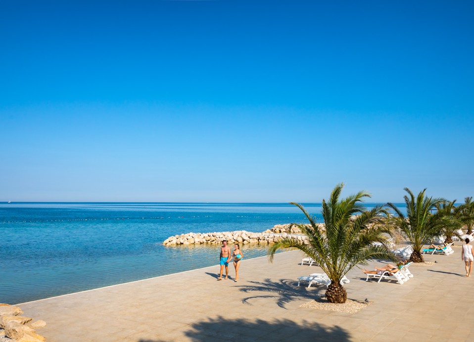 Passeggiata sul mare con palme e lettini al Maravea Resort vicino a Novigrad