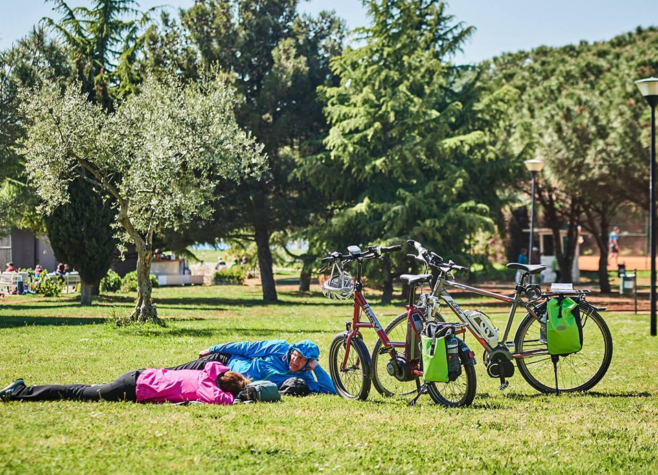 Radfahrer ruhen sich im Park des Campingplatzes Aminess Sirena in Novigrad neben ihren Fahrrädern aus.