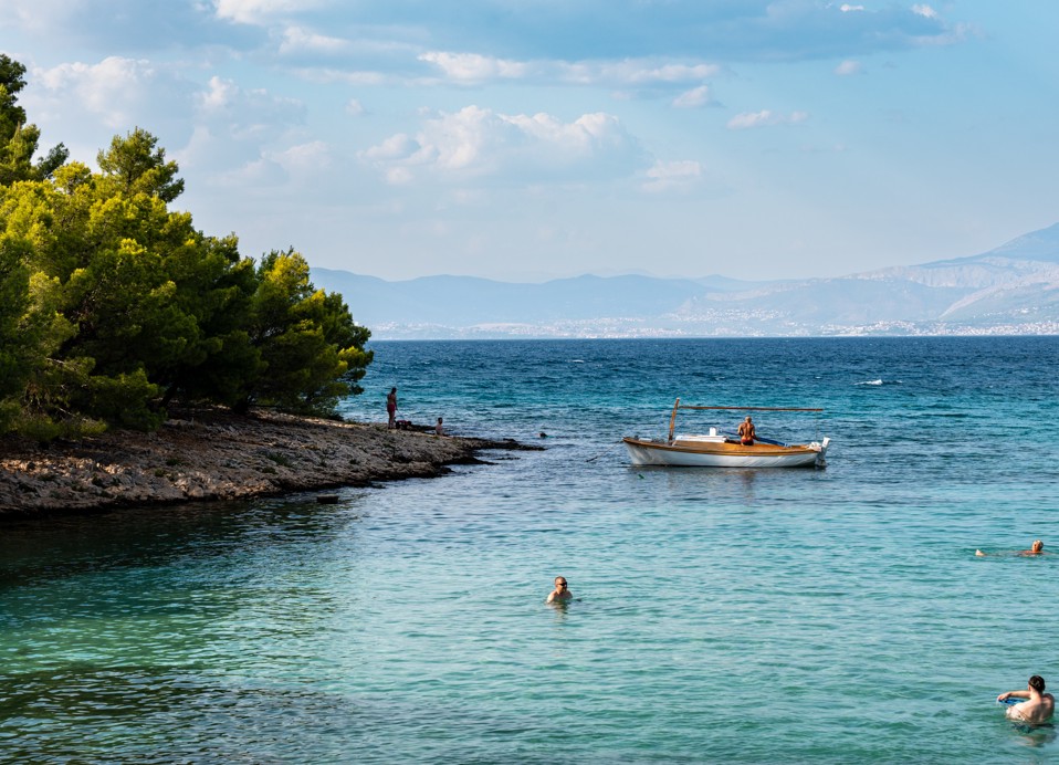 Mirna zaliv z kristalno čistim morjem, borovci in čolnom pred Aminess Vival Velaris Resortom na otoku Braču – popolno mesto za kopanje in sprostitev med poletnimi počitnicami na Hrvaškem.