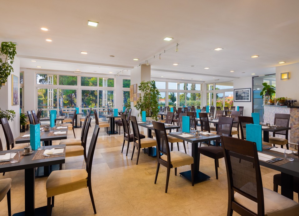 Notranjost restavracije Oliveto v Aminess Vival Velaris Resortu na otoku Brač z elegantnimi mizami, modernim dizajnom in pogledom na vrt skozi velika okna.