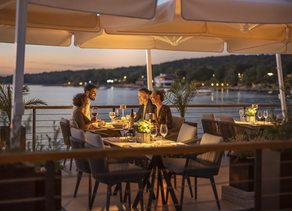 Skupina prijateljev uživa v večerji v restavraciji & baru 7 Seas blizu Aminess Style Camping Atea Resort, s čudovitim pogledom na sončni zahod.