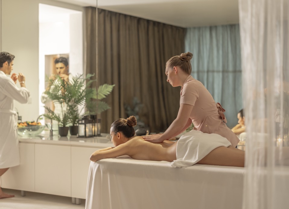 Koppel in een wellnessruimte voor twee, vrouw ontvangt een massage terwijl de man zijn gezicht wast.