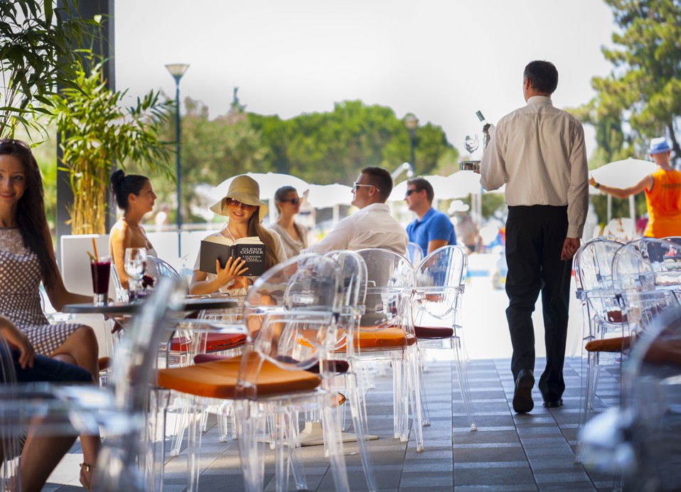 Mensen genieten van het buitenterras van de aperitiefbar, met een vrouw die een boek leest.