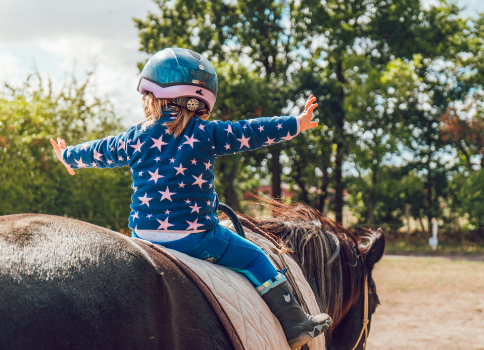 Kind beim Reiten im Aminess Atea Resort mit ausgestreckten Armen