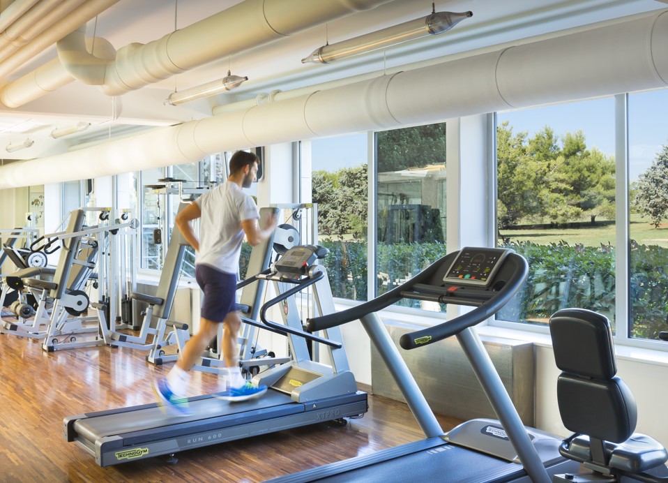 Een man op de loopband in de sportschool, met uitzicht op groen buiten.