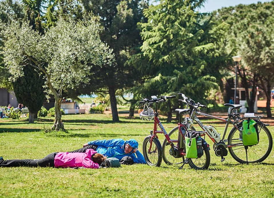 Ouder echtpaar liggend op het gras naast hun fietsen bij Aminess Planet Camping Maravea Resort, Novigrad Kroatië