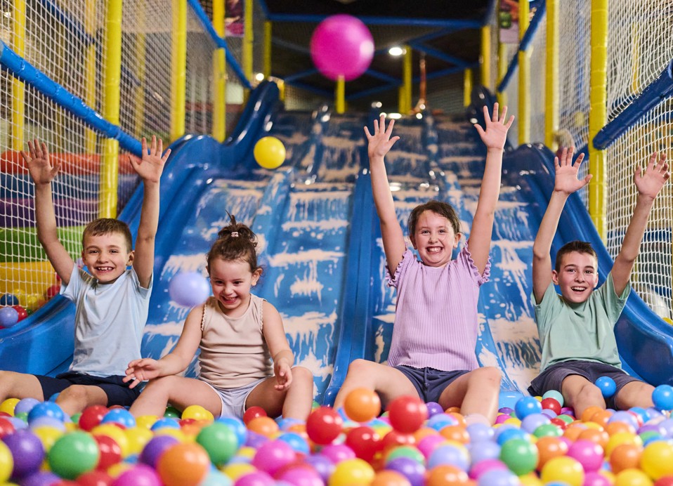 Kinderen glijden van een indoor glijbaan in een ballenbad in een speelruimte