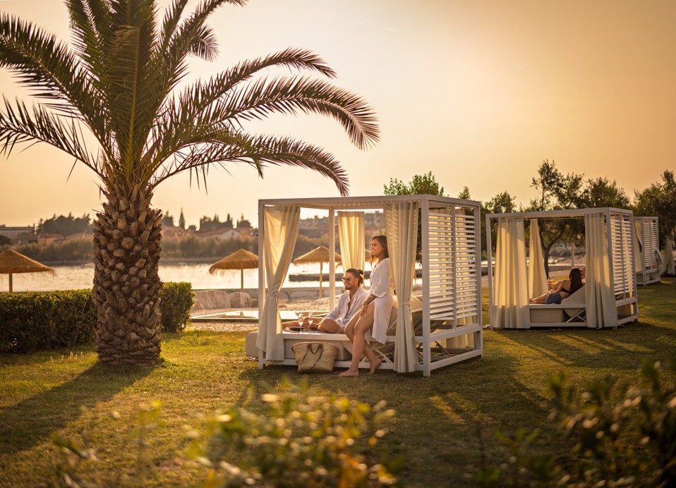 Guest relaxing in a private cabana surrounded by palm trees at the Aminess bar in Novigrad, Istria.