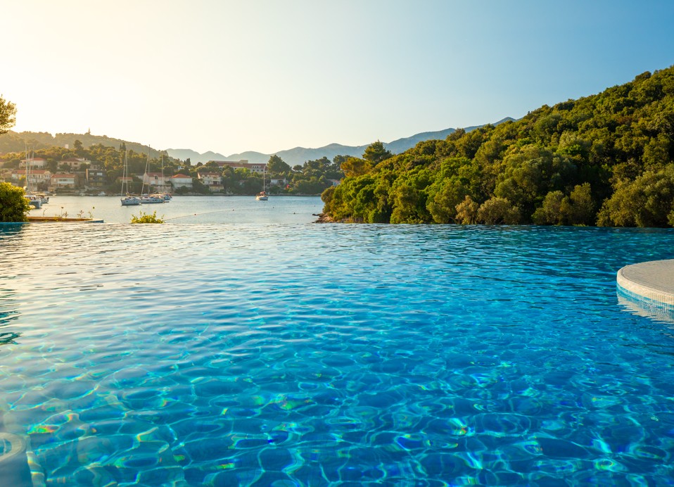 Blick über den sonnigen Pool auf den Strand vor dem Aminess Vival Port9 Resort.