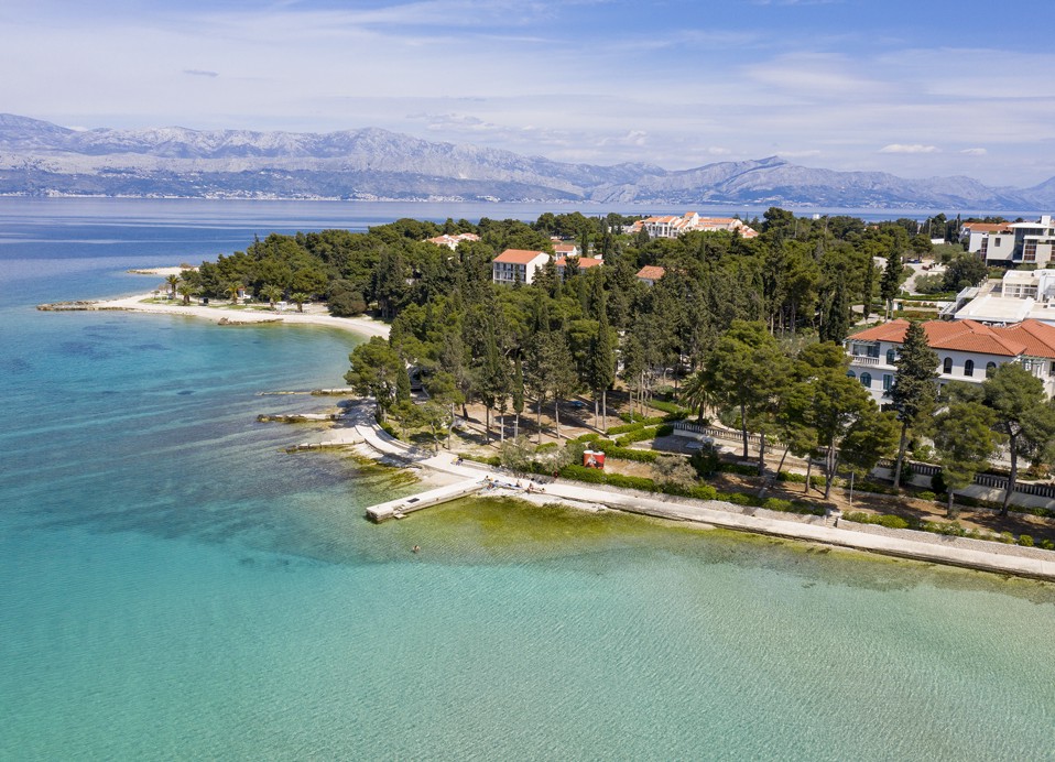 Zračni pogled na kristalno čisto morje, plažo in borov gozd ob Aminess Vival Velaris Resort na otoku Braču – popolno mesto za počitnice na hrvaški obali.