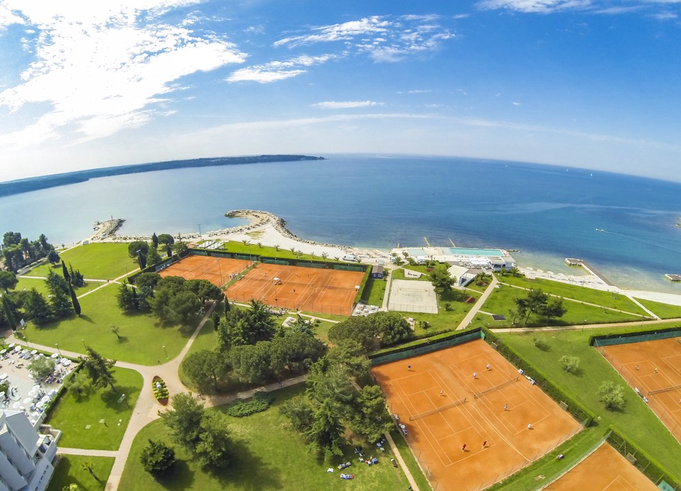 Vista aerea di tre campi da tennis sotto l'hotel Aminess Vival Maestral, con vista su Punto Mare e il mare.