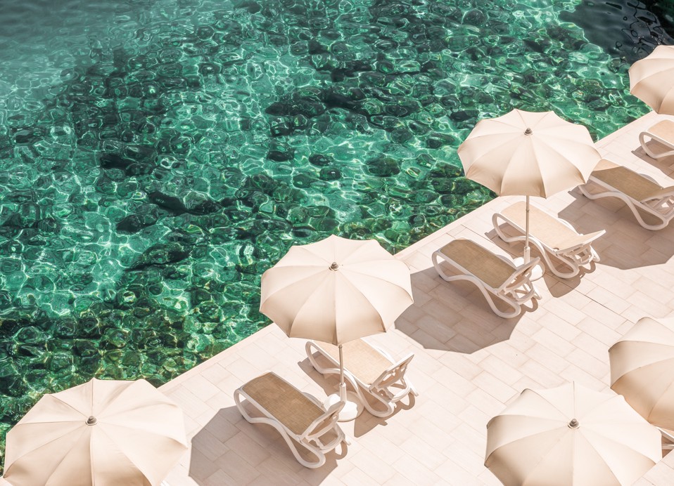 Sun loungers under umbrellas by the turquoise sea in front of Aminess Lume Hotel