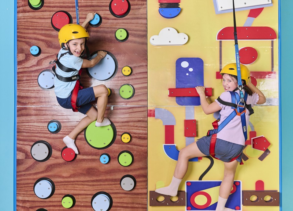 Kinderen met helmen klimmen op een indoor klimmuur in een speelruimte