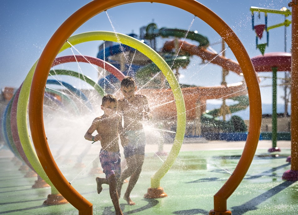 Kinder laufen durch die Wasserspritz-Zone im Aquapark